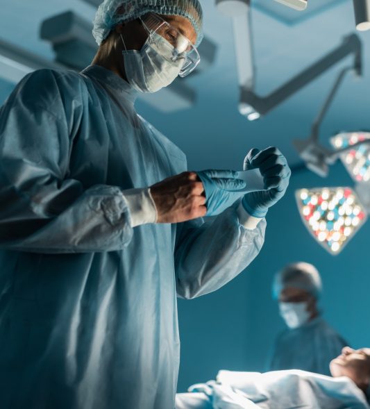 surgeon taking off medical gloves near patient in surgery room